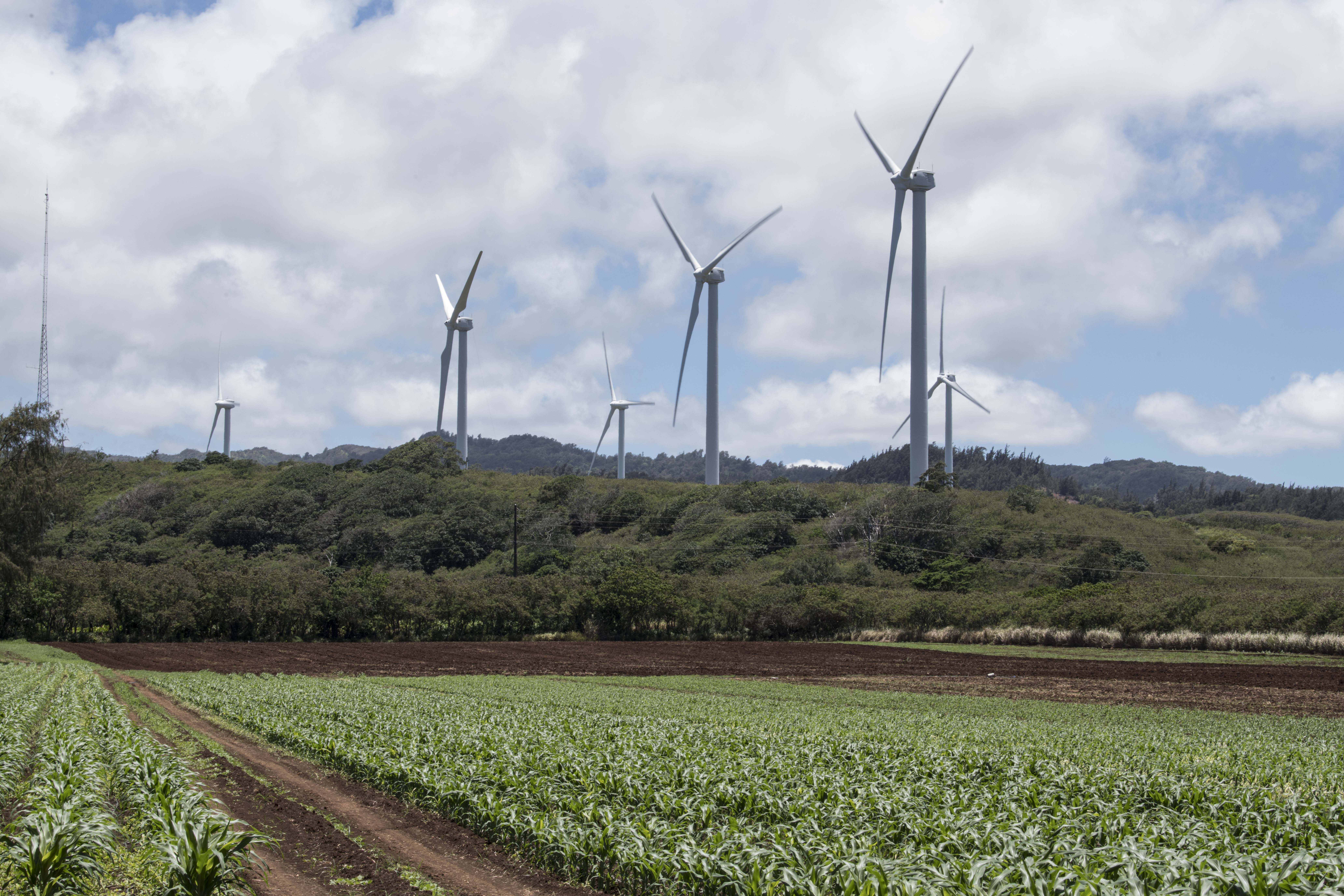 Several land-based wind turbines in front of an agricultural field and green hills