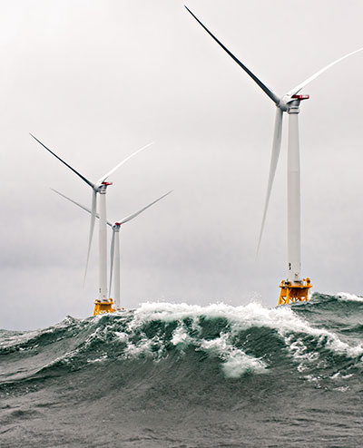 Several large, offshore wind turbines stand on large supports in a stormy ocean