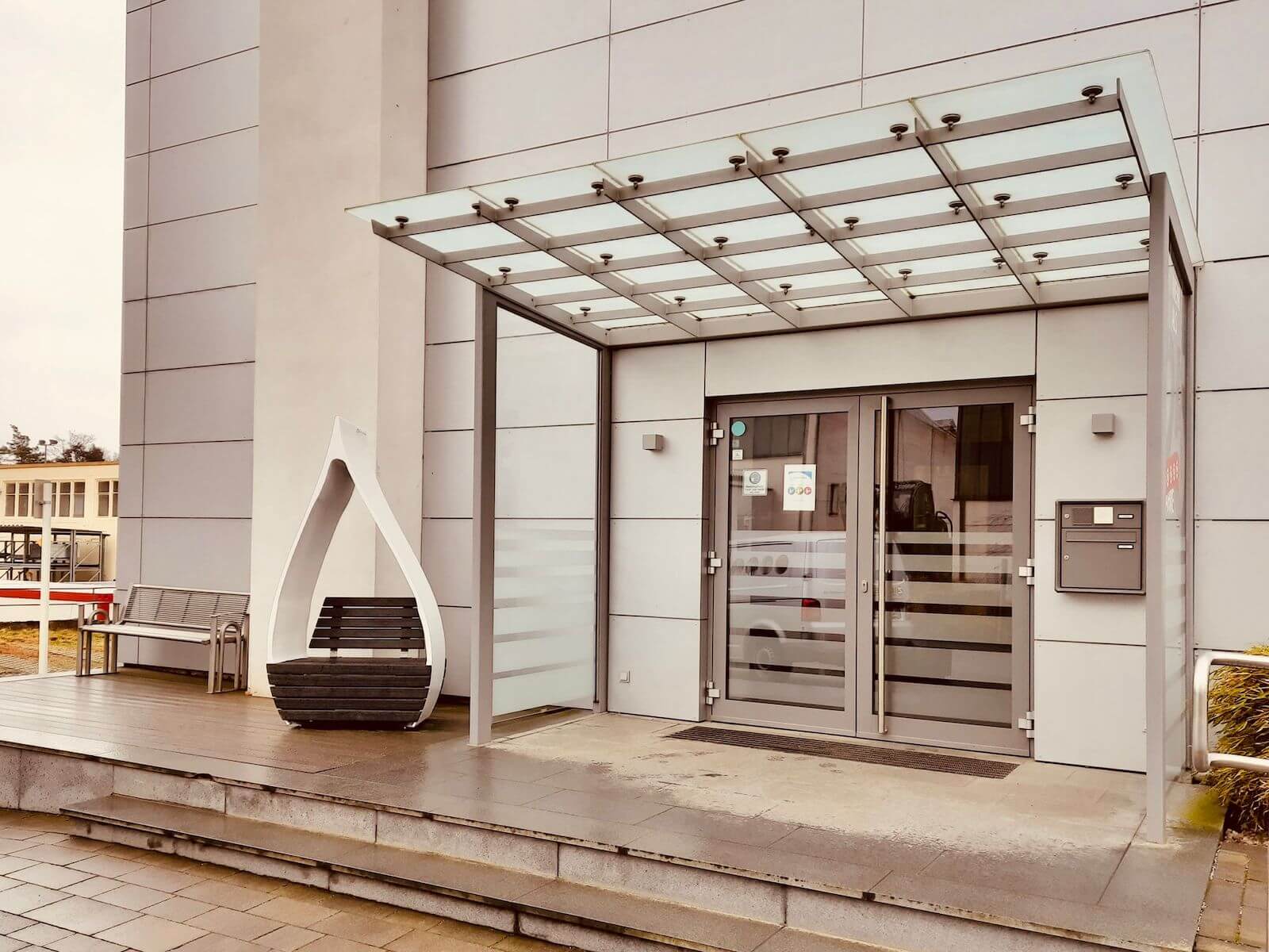 The front of a building with glass doors and a metal canopy at the top of two concrete steps.
