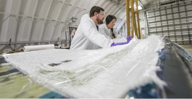Two people in protective gloves, goggles, and lab coats lay a material on a wind turbine mold.