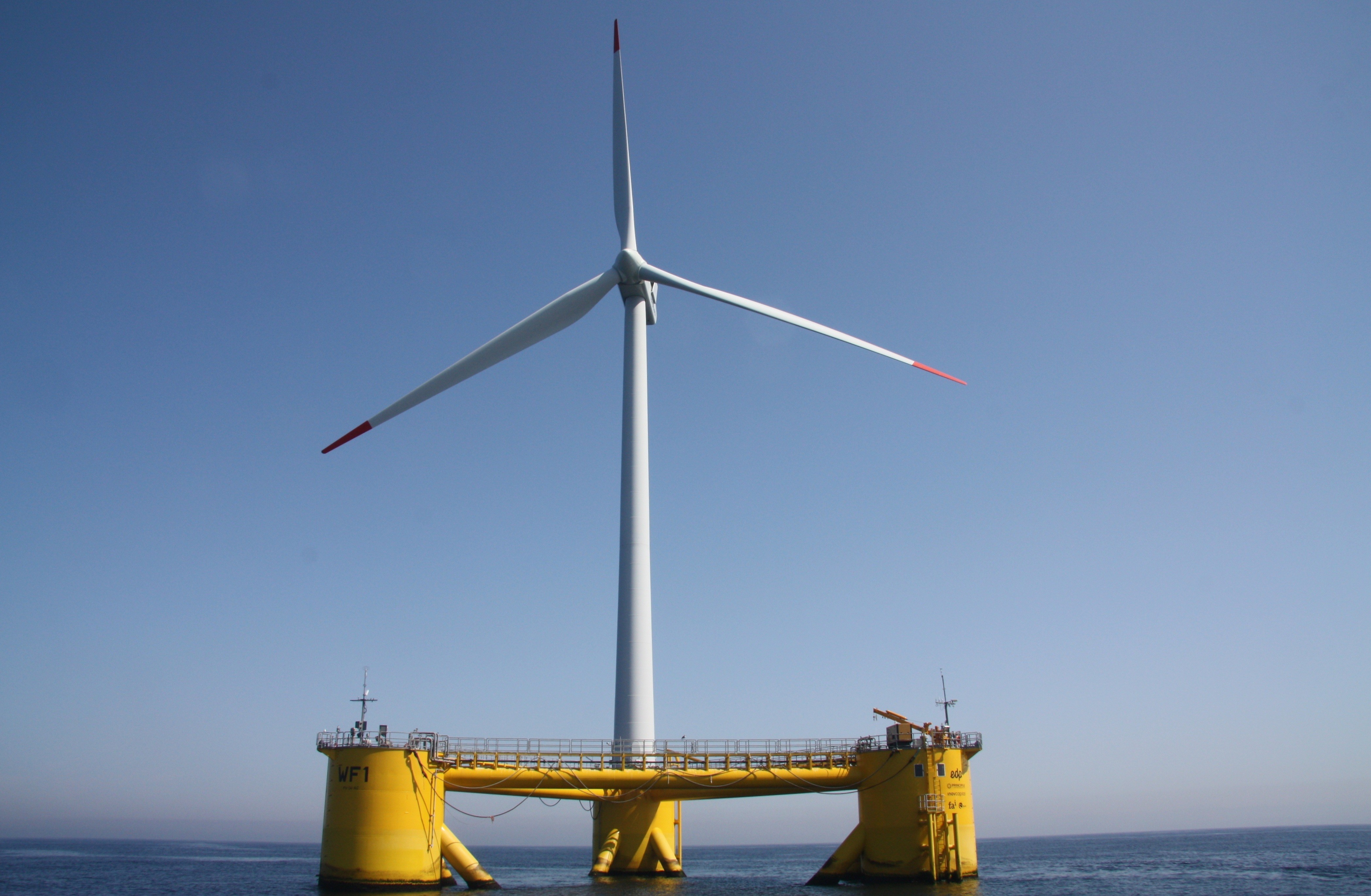 A wind turbine floating on a three-legged platform on the ocean.