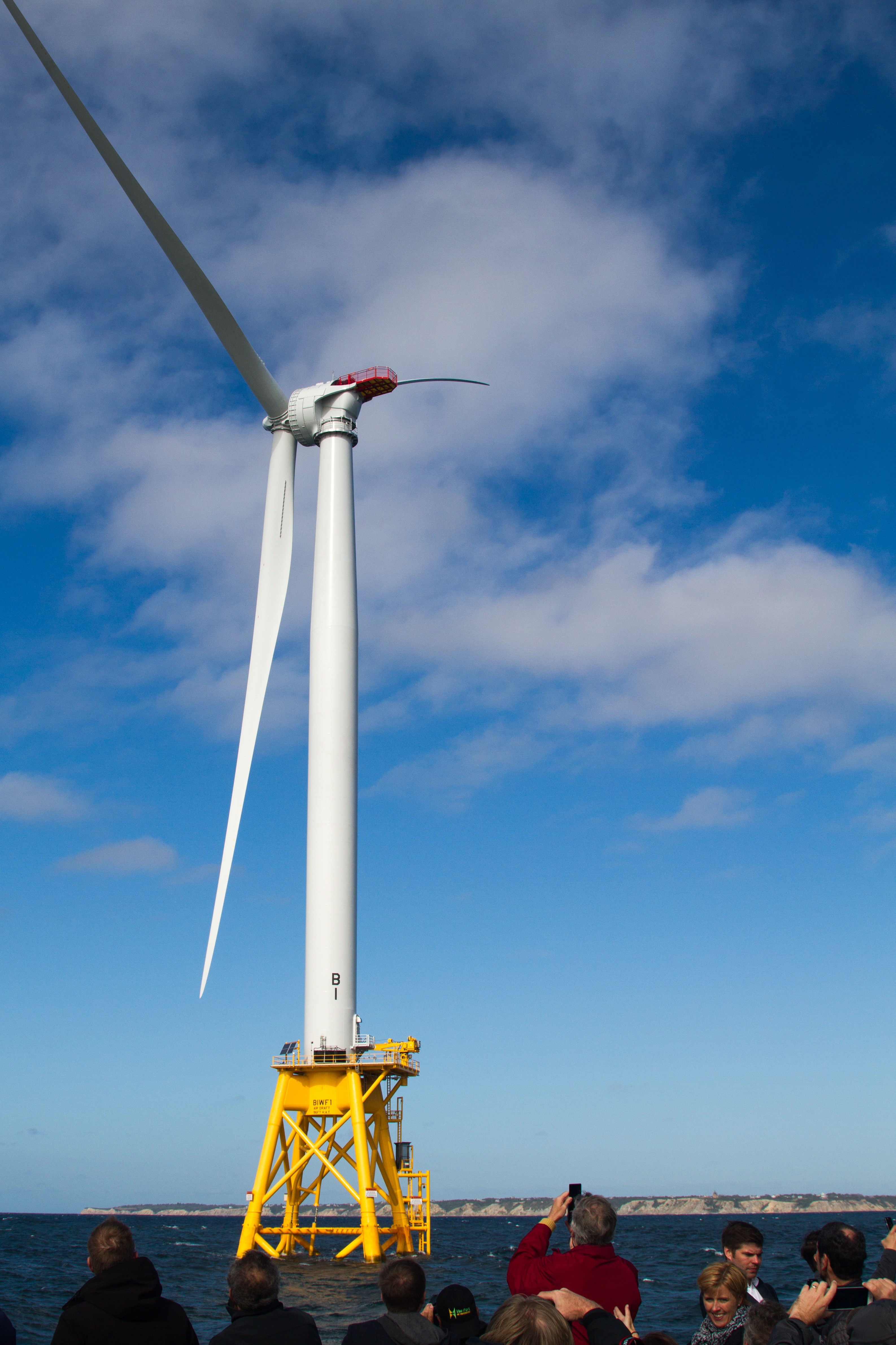 People on a boat photographinc a wind turbine.